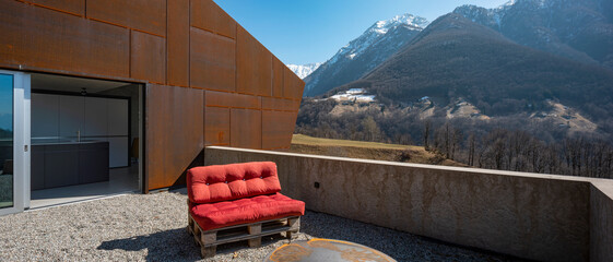 Modern house exteriors with veranda. Red sofa overlooking the mountains of Switzerland