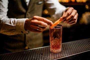 hands of barman carefully decorate clear crystal cocktail glass by fresh orange peel