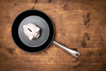 White piggy bank in a frying pan on wooden table