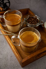 Iced Dalgona coffee drink on wooden tray background. Instant coffee or espresso powder whipped with sugar and hot water. Coffee with milk latte, cappuccino. Two glass cups with double walls. Breakfast