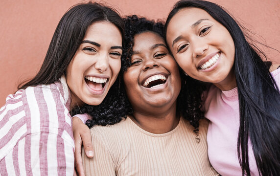 Happy latin women laughing and looking in camera - Millennial girls having fun outdoor taking a selfie