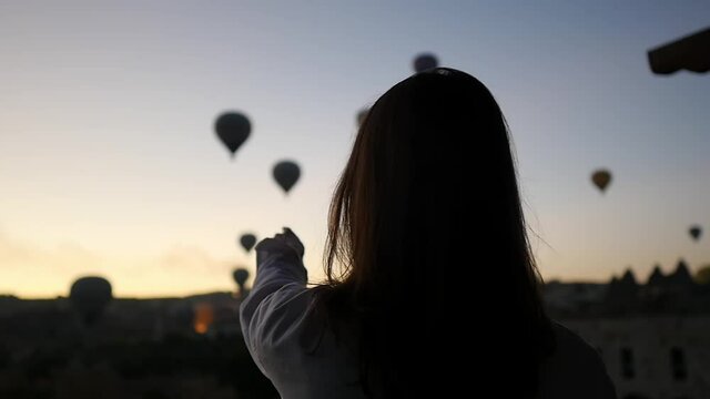 Woman traveler looking at balloons at sunrise. Feeling of complete freedom, achievement, achievement, happiness