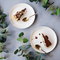 Two plates with cheesecake poured chocolate glaze. Plates on table decorated green leaves. Sweet food background. Top view.