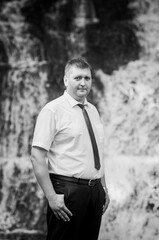 The groom stands against the background of a waterfall