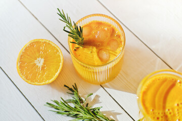 fresh squeezed iced orange juice and half of an orange on white table. rosemary leaves in a glass with juice. top view. vitamin and antioxidant drinks