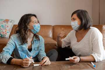 Two women in protective face mask sitting together performing a self Antigen test for COVID-19 at...