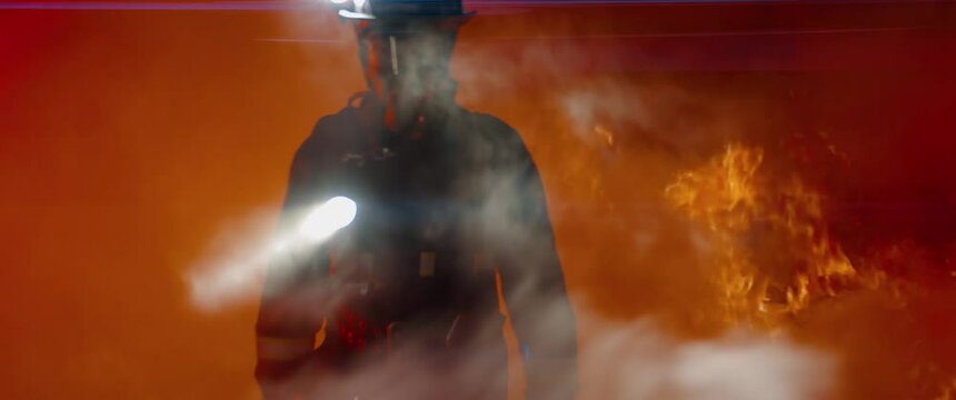 Dramatic shot of American firefighter in full gear walking through smoke away from fire. Shot with 2x anamorphic lens 
