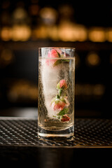 close-up on glass with drink and large ice cube in which frozen pink rosebuds