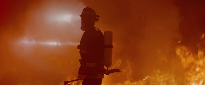 Dramatic silhouette of American firefighter in full gear exploring the huge fire zone. Shot with 2x anamorphic lens 
