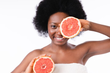 Cheerful african young girl in spa towel holding grapefruits isolated in white