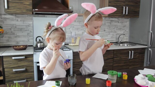 teenagers a boy and a girl in rabbit ears draw Easter eggs in the kitchen in preparation for the Easter holiday