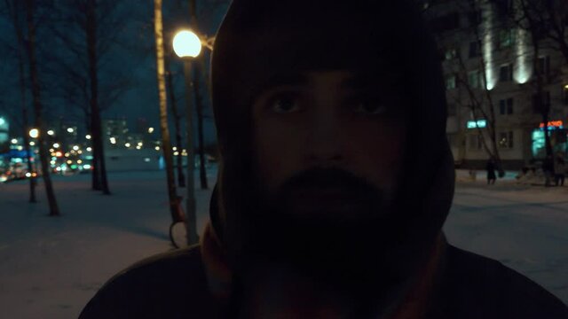 Moody scene of Man walking on dark cold winter streets in frozen Russia at night. He wears winter clothes and tries to stay alive, warm himself and drive away crawling depression of the dark windows