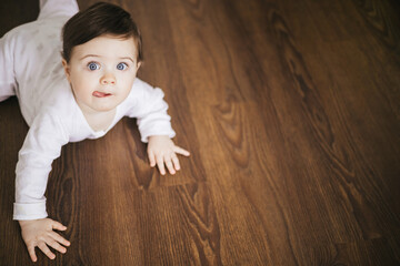 Little baby boy crawling on wooden floor and smiling with copy space