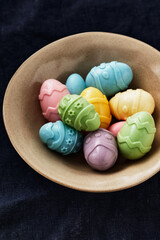 Multicolored Chocolate Candy Speckled Easter Eggs on Plate on Tabletop. One Bitten Off. Holiday Poster Banner Template with Copy Space for Text.