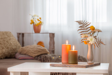 Fototapeta na wymiar burning candles with autumn decor on white table at home