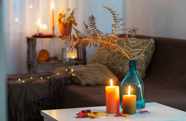 burning candles with autumn decor on white table at home
