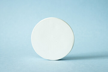 White cocncrete circle shaped pedestal on blue background, side view. Podium mockup background for products. Advertising template. Stone platform. Abstract geometric pedestal