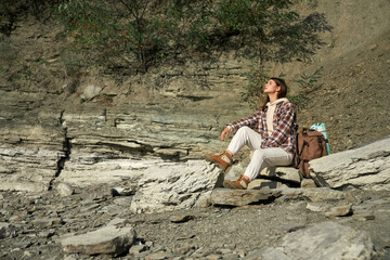 Happy woman sitting on stone and enjoying sunny weather