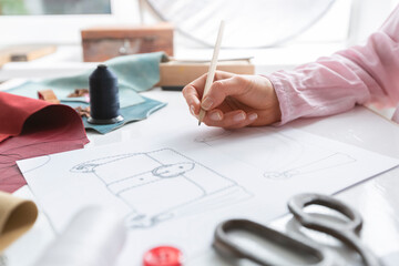 The designer draws a sketch of a woman's bag on paper at the workplace. Fashion design.