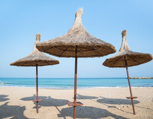 Summer landscape with straw umbrellas on the beach in Mangalia or Mamaia. Beach at the Black Sea in Romania.
