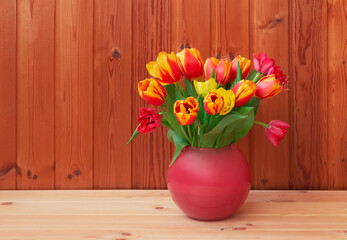 Bouquet of fresh tulips in vase on wooden table.
