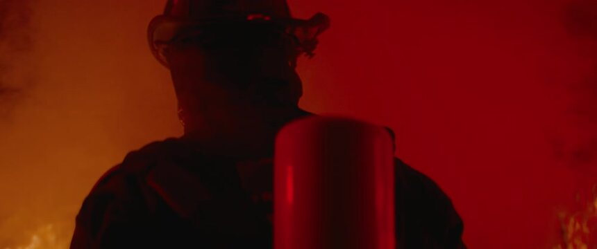 HANDHELD TRACKING Dramatic shot of American firefighter in full gear walking into smoke and huge fire. Shot with 2x anamorphic lens 