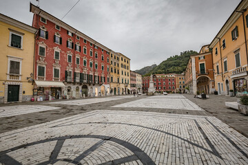 Fototapeta na wymiar Cityscape. Carrara city center: Piazza Alberica with the commemorative monument in the center and the Ducal Palace , and small open doors cafes, shops in Tuscany, Italy