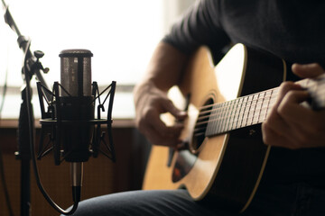 Man playing acoustic guitar and recording with a microphone in a room. Home studio