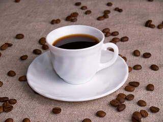 A white espresso cup stands on a burlap table with scattered coffee beans.