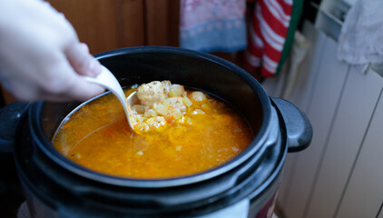 woman stirring with a plastic scoop the soup with meatballs cooked in a slow cooker