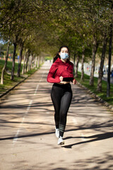 Fototapeta premium Young woman with face mask because covid, running in the park. Active person outdoors.