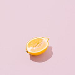 Lemon half on a pale pink background. Sunlit vintage yellow summer fruit with shadow. Retro beach food aesthetic layout.