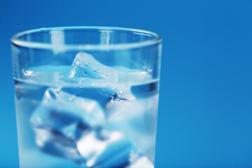 A glass with ice water and ice cubes on a blue background.