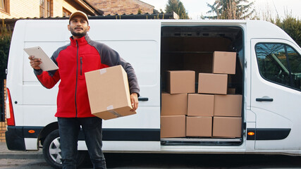 Young man delivering package. Using tablet to read the order. High quality photo