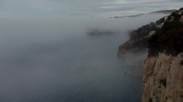 Flying over the cliff on a foggy day. At the ned a house appears at the top of the cliff