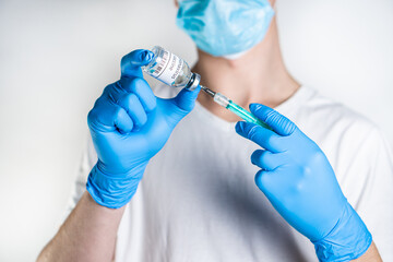 The doctor takes the coronavirus vaccine in a syringe. He has blue rubber gloves on his hands, which serve as protection against coronavirus infection.