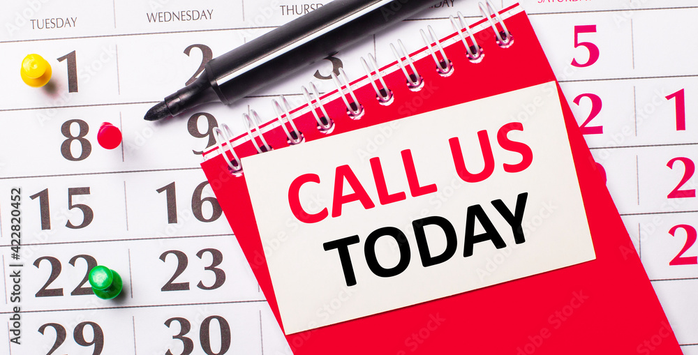 Poster on the calendar is a white card with the text call us today. nearby is a red notepad and a marker. v