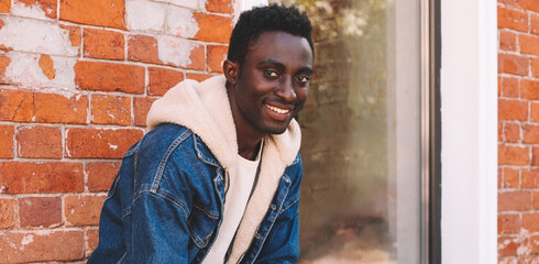 Portrait of stylish happy smiling young african man on a city street over brick wall background