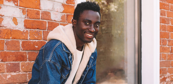 Portrait of stylish happy smiling young african man on a city street over brick wall background