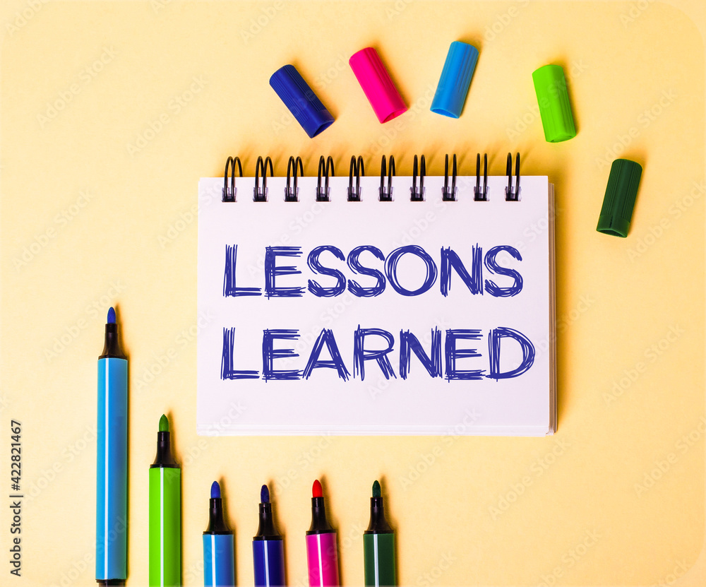 Poster the words lessons learned written in a white notebook on a beige background near multi-colored marke