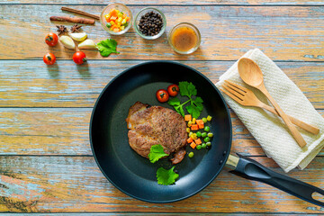 Grilled beef steak and roasted vegetables on dark wooden table background, top view. Juicy meat dish with sauce, rosemary, peppers and cutlery in fry pan. Restaurant food