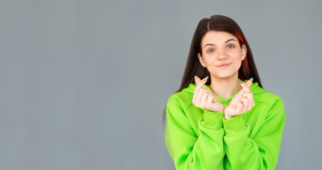Romantic woman shows korean heart sign with two fingers crossed, smiles joyfully and confesses in...