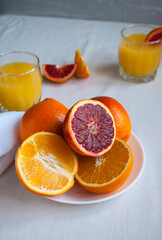 Sweet and juicy blood oranges and oranges, whole and cut on a white plate and glasses of fresh orange juice. Fresh orange juice with Sliced oranges.