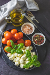 Mozzarella cheese, basil and tomato cherry in oval black plate, copy space. Ingredients for Caprese salad