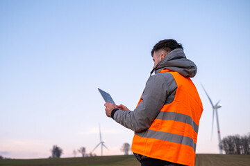 Windmill engineer does maintenance and repairs wind turbines using a tablet in the orange vesta.