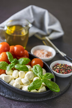 Mozzarella cheese, basil and tomato cherry in oval black plate, copy space. Ingredients for Caprese salad