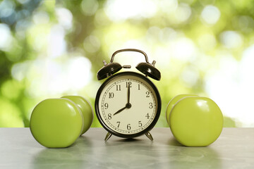 Alarm clock and dumbbells on marble table outdoors. Morning exercise