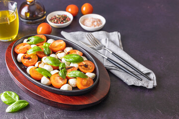 Caprese salad with cherry tomatoes, mozzarella and basil in oval black plate