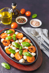 Caprese salad with cherry tomatoes, mozzarella and basil in oval black plate