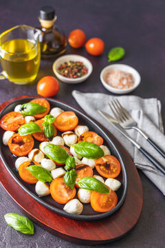 Caprese salad with cherry tomatoes, mozzarella and basil in oval black plate